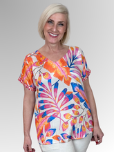 Inject a vibrant energy into your seasonal style with the Julia V-Neck Top by Escape. This stunning pullover top displays an artistic tropical design exploding with punchy shades of orange, magenta, and royal blue against a fresh cream background, balanced by an ornamental printed trim along the cuffs. Cut from premium, silky-soft rayon, it drops over the silhouette with a fluid, lightweight motion that guarantees maximum airflow and comfort during warmer months.
