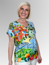 Capture the essence of a European holiday with the Adele V-Neck Top by Escape. This charming pullover tee showcases a picturesque Italian coastal scene complete with colourful cliffside villas, sun-drenched beaches, and retro umbrellas, balanced by vibrant citrus fruits and "Dolce Vita" typography details. Cut from premium, silky-soft rayon, it drapes the figure with a fluid, featherweight movement that promises exceptional breathability and absolute comfort through the warmest days.