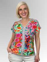 Capture a sense of natural beauty with the Songbird V-Neck Top by Escape. Woven from a premium blend of cotton, rayon, and spandex, this lightweight tee delivers an easy, unrestricted drape with plenty of comfortable give. It features an exquisite botanical print showcasing vibrant songbirds and hummingbirds nestled amidst lush tropical flowers, rich greenery, and warm orange-pink skies.
