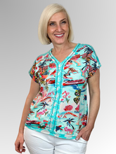 Bring a relaxed, holiday vibe to your casual wardrobe with the Bahamas V-Neck Top by Escape. Woven from a premium blend of cotton, rayon, and spandex, this top feels wonderfully soft against the skin while offering a breezy, unstructured drape and an easy, comfortable fit. It features a cheerful, postcard-style Bahamas beachside scene print complete with swaying palm trees, pink flamingos, cruise boats, and sun loungers set against an aqua and coral background.