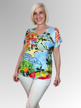Capture the essence of a European holiday with the Adele V-Neck Top by Escape. This charming pullover tee showcases a picturesque Italian coastal scene complete with colourful cliffside villas, sun-drenched beaches, and retro umbrellas, balanced by vibrant citrus fruits and "Dolce Vita" typography details. Cut from premium, silky-soft rayon, it drapes the figure with a fluid, featherweight movement that promises exceptional breathability and absolute comfort through the warmest days.