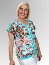 Bring a relaxed, holiday vibe to your casual wardrobe with the Bahamas V-Neck Top by Escape. Woven from a premium blend of cotton, rayon, and spandex, this top feels wonderfully soft against the skin while offering a breezy, unstructured drape and an easy, comfortable fit. It features a cheerful, postcard-style Bahamas beachside scene print complete with swaying palm trees, pink flamingos, cruise boats, and sun loungers set against an aqua and coral background.