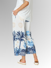 Embrace effortless summer style with the Azure Escape Print Pant, a striking statement piece designed for relaxed, warm-weather dressing. Showcasing a beautiful, resort-inspired print featuring classic palm motifs and ornate blue patterns against a crisp white background, these wide-leg pants inject modern colour and fluid movement into your everyday wardrobe. Crafted from a premium blend of Viscose and Nylon, the subtly textured fabric provides an airy, lightweight feel that is perfect for balmy climates.